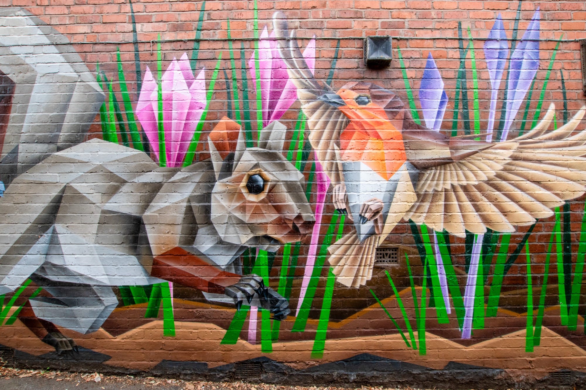 A brick wall mural by Anatomyx depicts squirrels, flowers, and a flying robin.