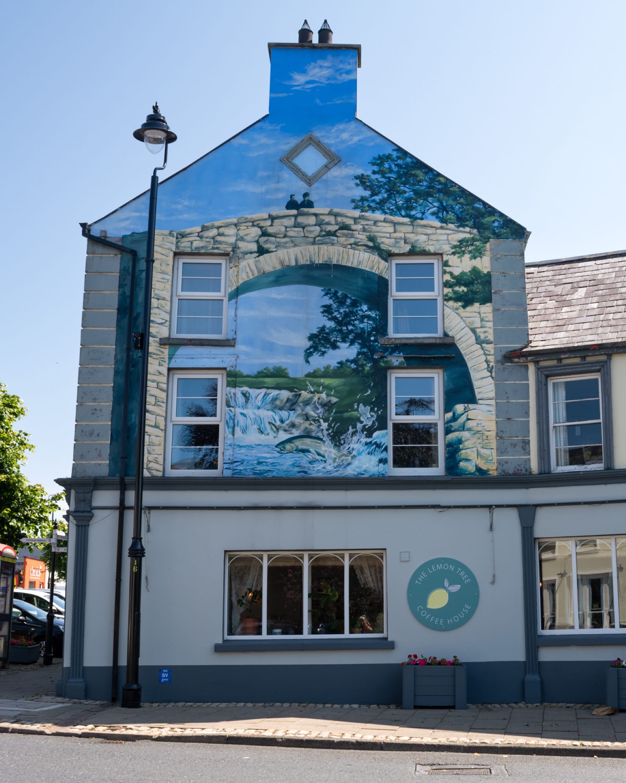A mural on the edge of the building depicts a trompe l'oeil scene of crumbling architecture against a blue sky.