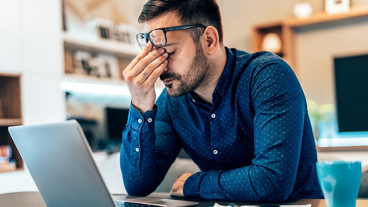 Tired young businessman working from home using laptop and looking anxious