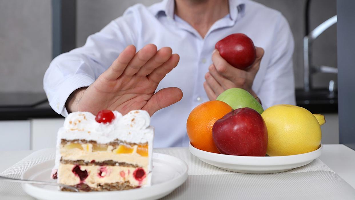 A man refuses to eat unhealthy cake or choose fruit for dessert. Healthy eating and active lifestyle concept