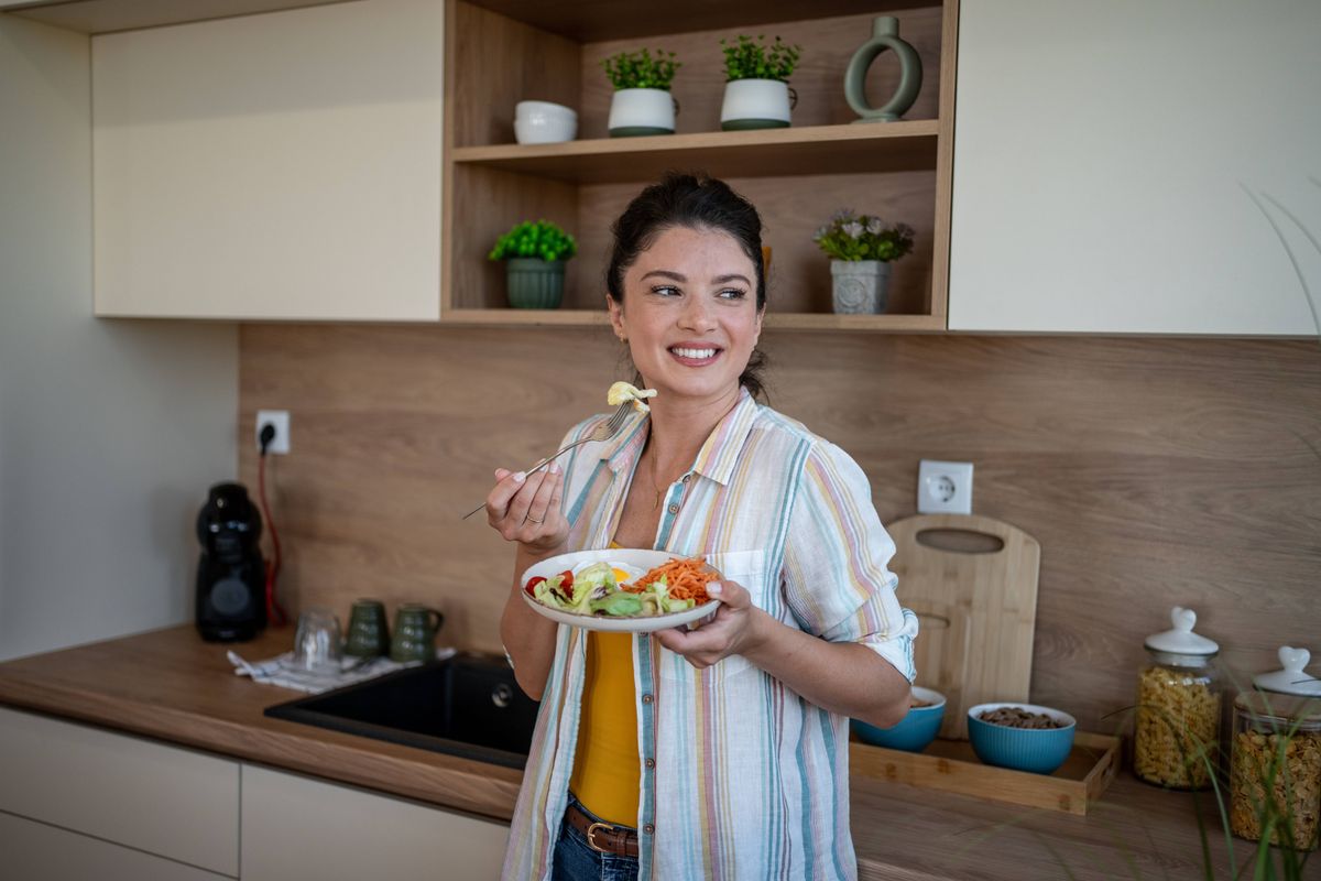 Cheerful woman enjoying colorful and nutritious salad in modern kitchen, celebrating healthy lifestyle and enjoying the taste of fresh vegetables and healthy ingredients