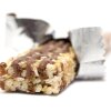 This photo shows a granola bar with the wrapper opened and partially pulled back. It is lying on a white surface and a white background.
