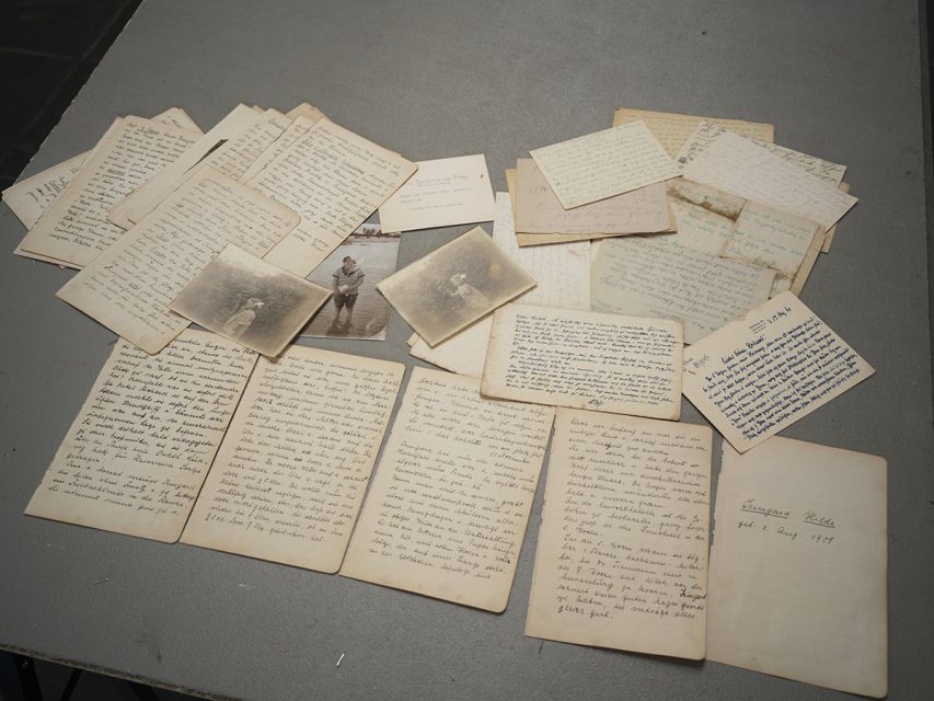 A collection of handwritten letters and old black and white photos spread out on a gray tabletop.