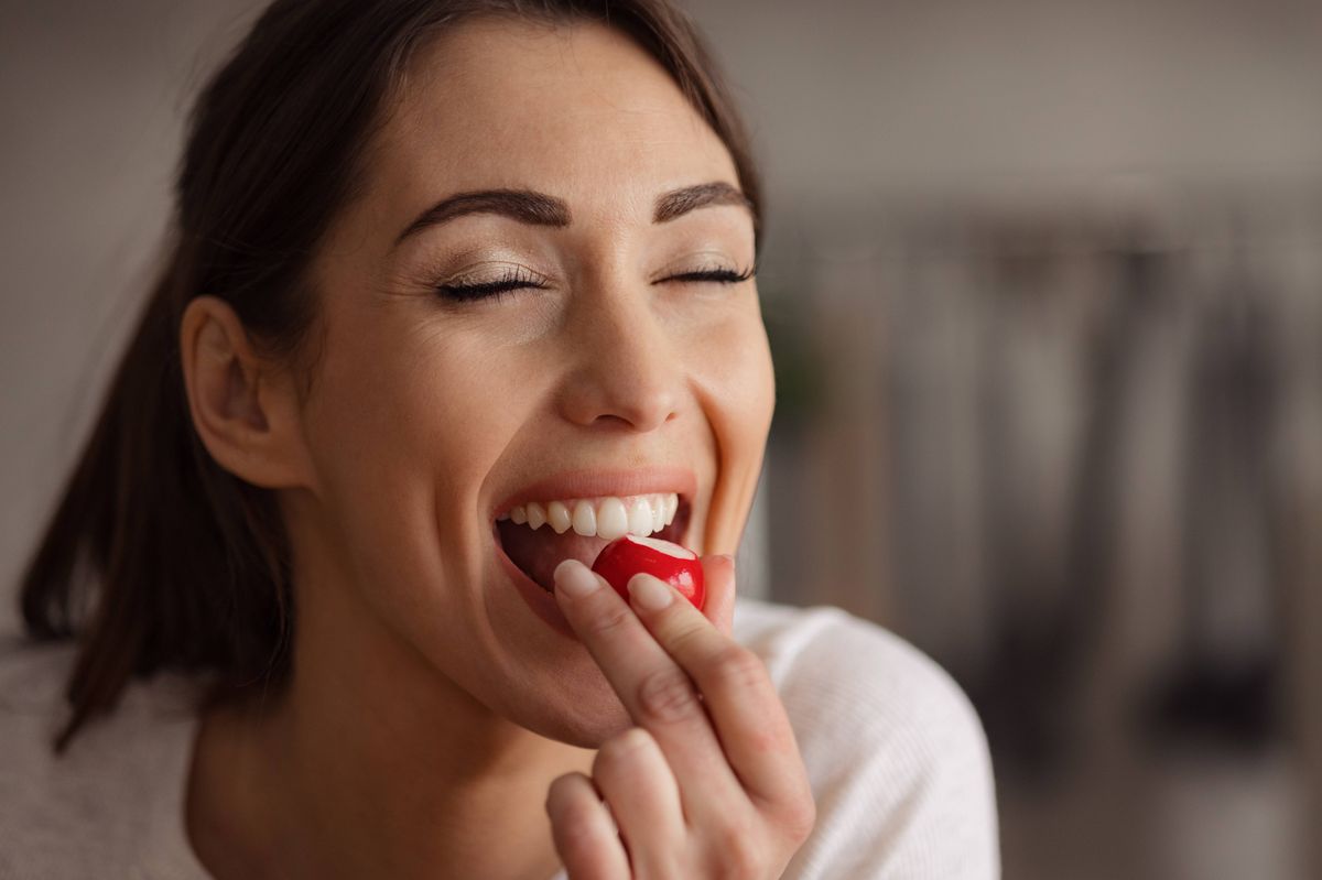 Portrait of happy woman enjoying while eating fresh radish with eyes closed at home.