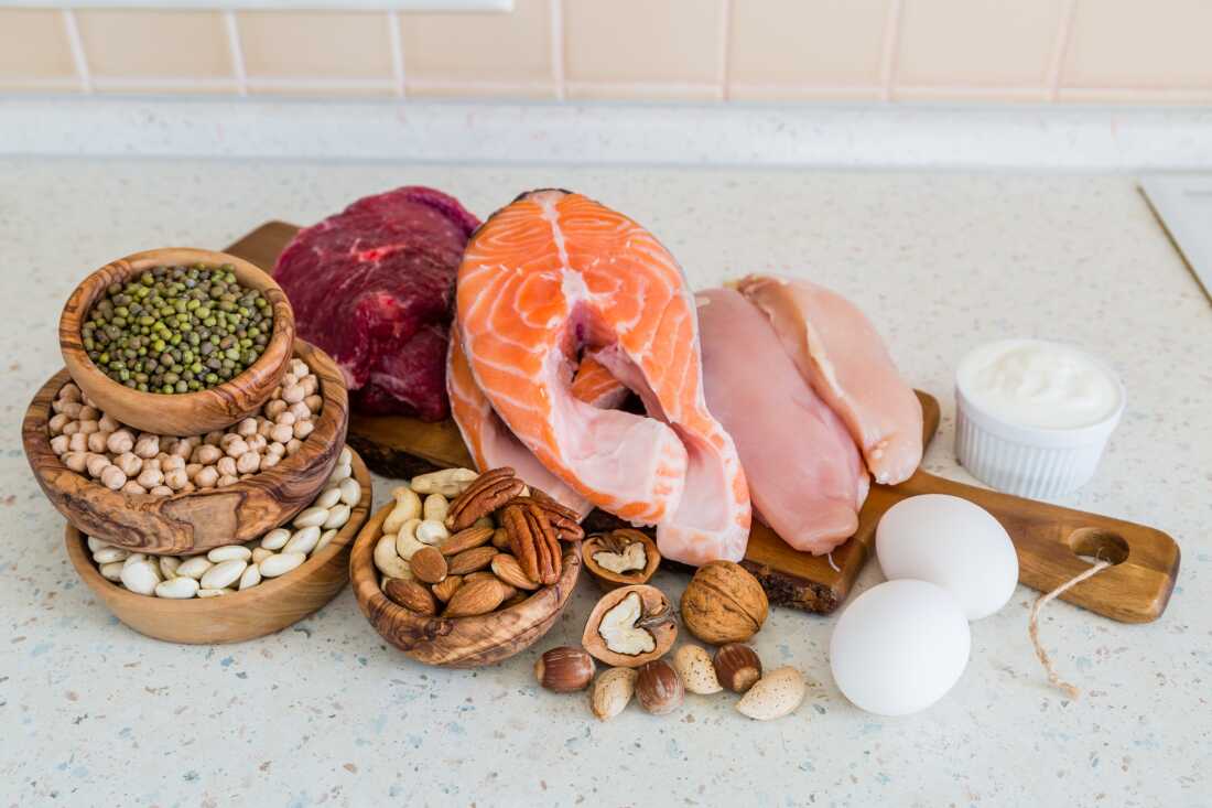 A selection of nuts, beans, eggs, raw chicken, fish and beef are arranged on wooden boards and bowls on the counter.