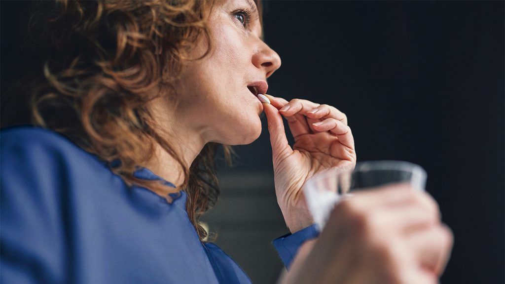 Woman preparing to swallow vitamin D supplement with glass of water in hand