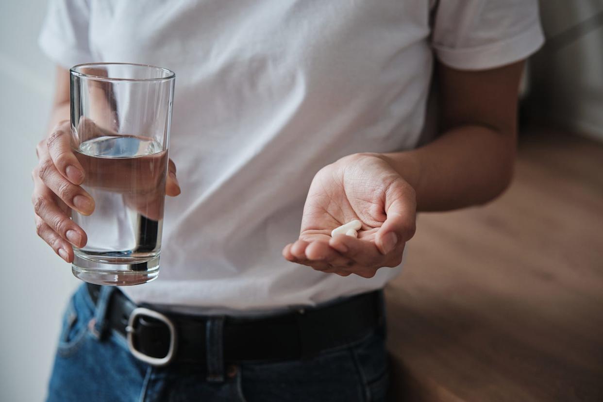 Woman holding pills and glass of water while standing in kitchen at home, cropped photo, people taking daily vitamins and treating illnesses Mental health medications, multivitamins, nutritional supplements