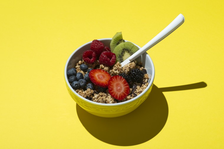 Bowl with muesli, chocolate and fruit on yellow background