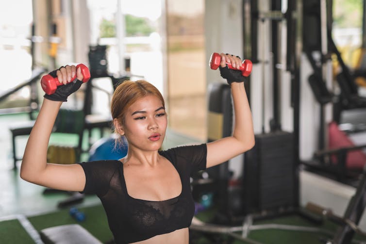 A woman doing dumbbell presses while sitting at the gym.
